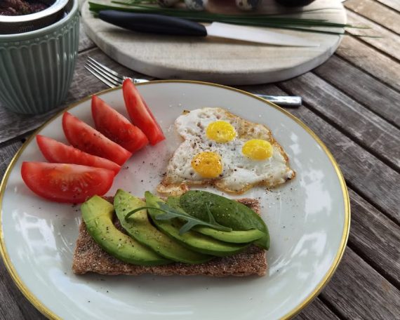 A vibrant outdoor breakfast setup with avocado toast, quail eggs, tomatoes, and tea.